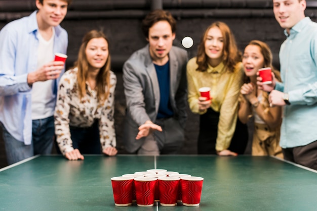 Friends looking at ball while man playing beer pong in bar