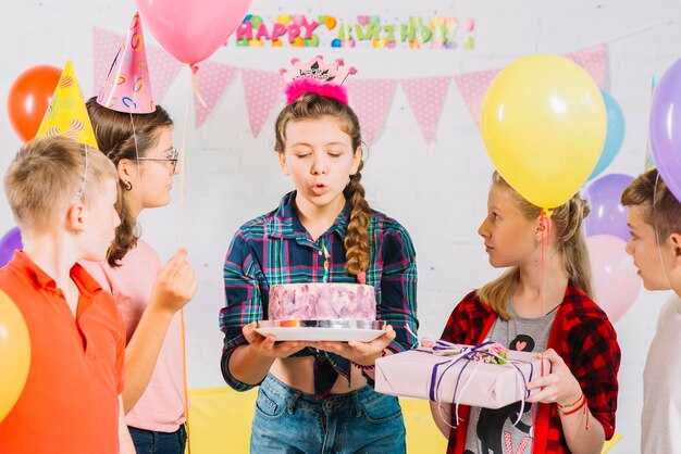 Friends looking at girl with birthday cake blowing candle