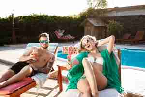 Foto gratuita amici sdraiati su sedie a sdraio vicino alla piscina, facendo selfie, sorridendo