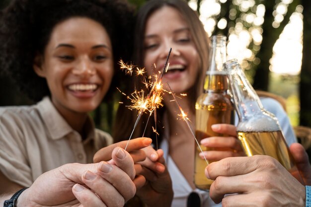Друзья на открытом воздухе в парке пьют пиво и наслаждаются бенгальскими огнями