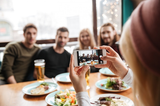 Gli amici che si siedono in caffè e che bevono l'alcool e fanno la foto