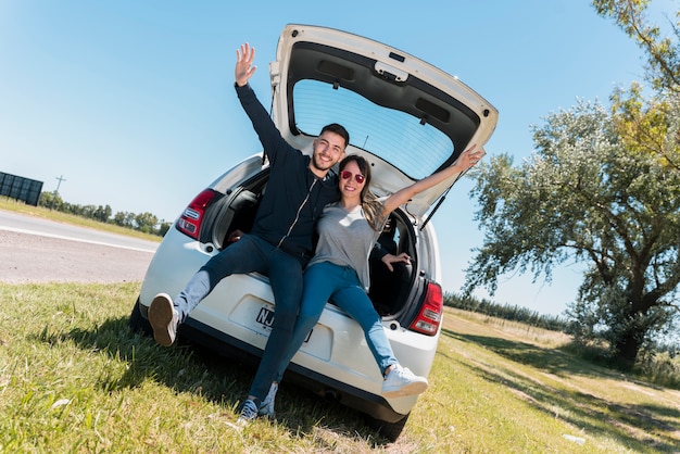 Friends sitting on car trunk making peace sign