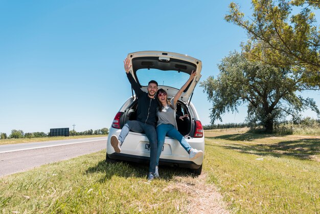 Friends sitting on car trunk making peace sign