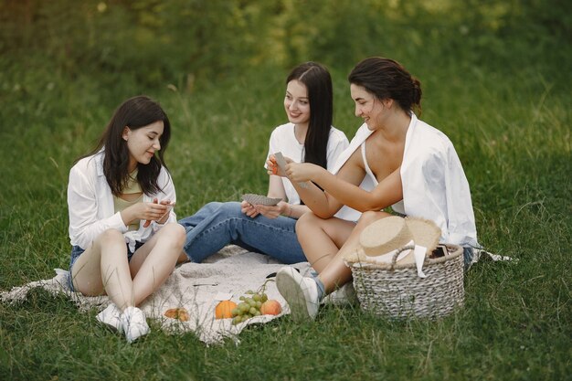 Friends sitting on a grass. Girls on a blanket. Woman in a white shirt.