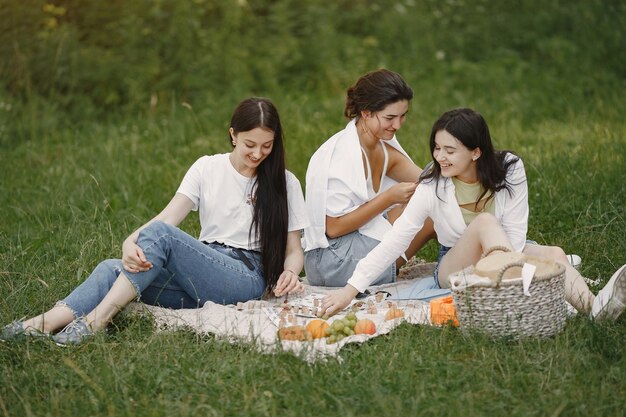 Friends sitting on a grass. Girls on a blanket. Woman in a white shirt.