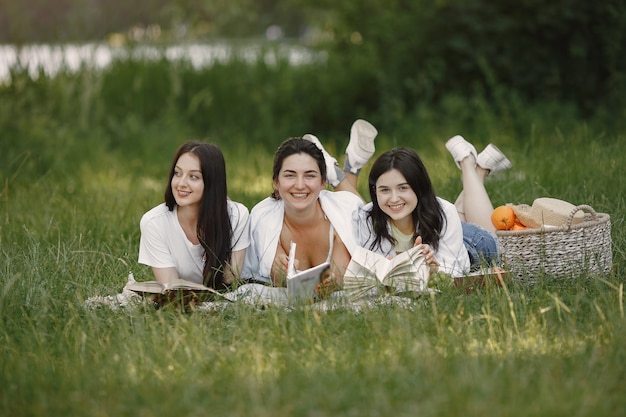 Friends sitting on a grass. Girls on a blanket. Woman in a white shirt.
