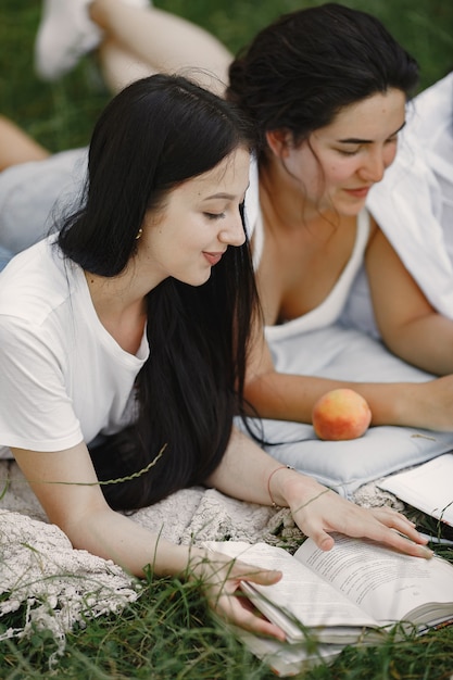 Free photo friends sitting on a grass. girls on a blanket. woman in a white shirt.