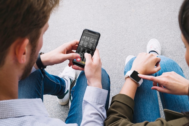 Friends sitting on street connecting smart watch with mobile phone
