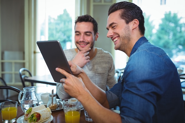 Friends sitting at table and using digital tablet in cafÃ©