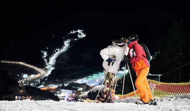 Друзья-лыжники веселятся на горнолыжном курорте в горах зимой, катаются на лыжах ночью