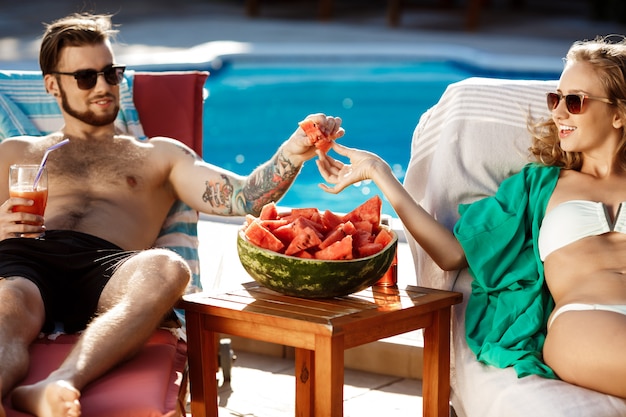 Foto gratuita amici che sorridono, bevendo cocktail, sdraiati su sedie a sdraio vicino alla piscina