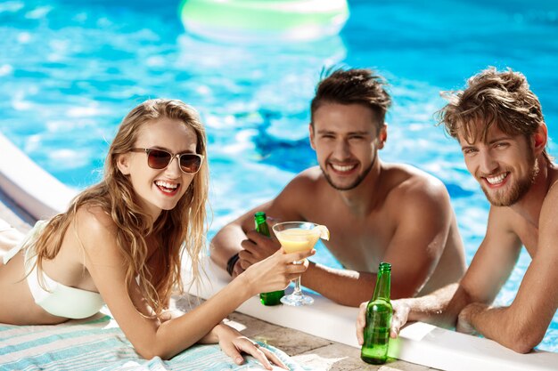 Friends speaking, smiling, drinking cocktails, resting, relaxing near swimming pool