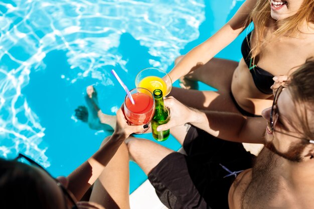 Friends speaking, smiling, drinking cocktails, resting, relaxing near swimming pool