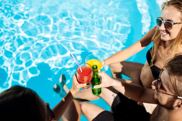 Friends speaking, smiling, drinking cocktails, resting, relaxing near swimming pool