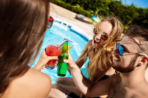 Friends speaking, smiling, drinking cocktails, resting, relaxing near swimming pool