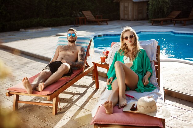 Friends sunbathing, lying on chaises near swimming pool