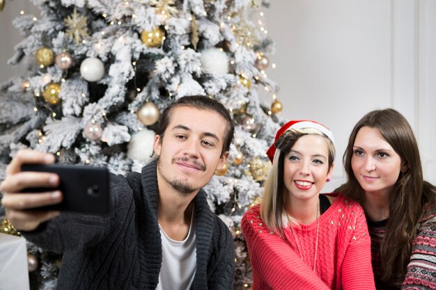 Friends taking selfie in front of christmas tree