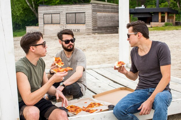 Friends talking and eating pizza on beach