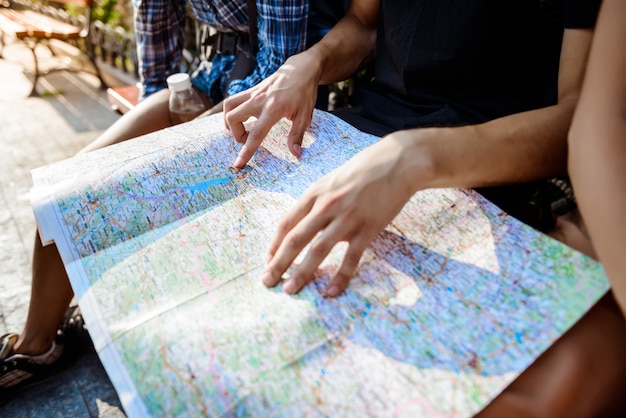 Friends travelers smiling, looking route at map, sitting on bench.