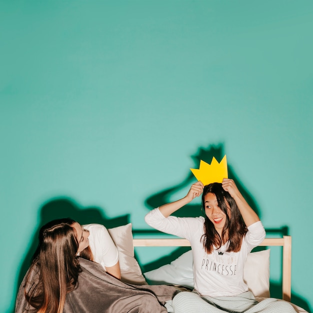 Friends trying on paper crown in bed