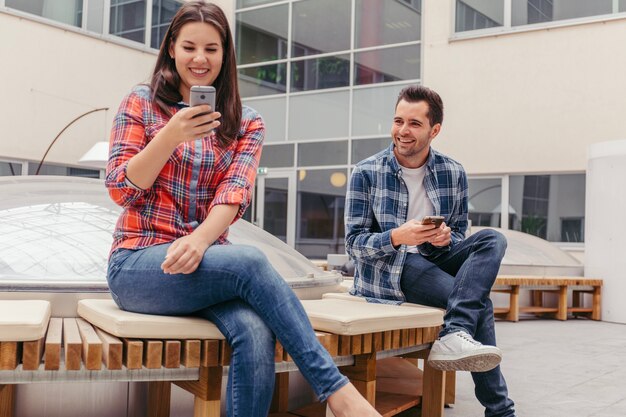 Friends using phones and sitting on bench