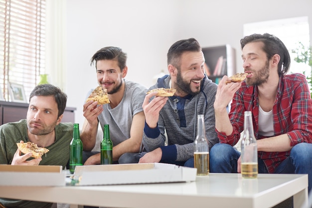 Friends watching TV and eating pizza