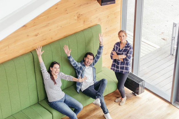 Friends waving at camera on sofa