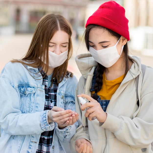 Free photo friends with mask using hand sanitizer