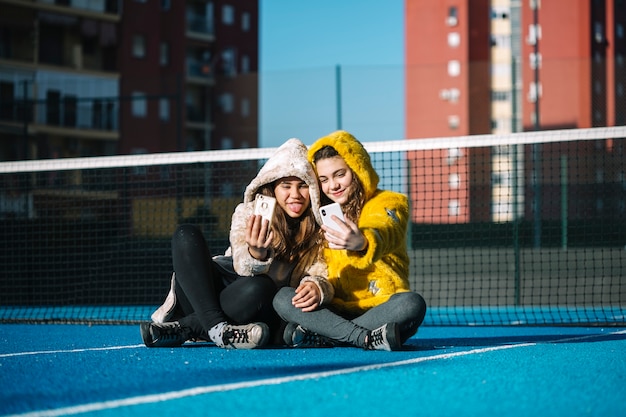 Friendship concept of two girls taking selfie on tennis court