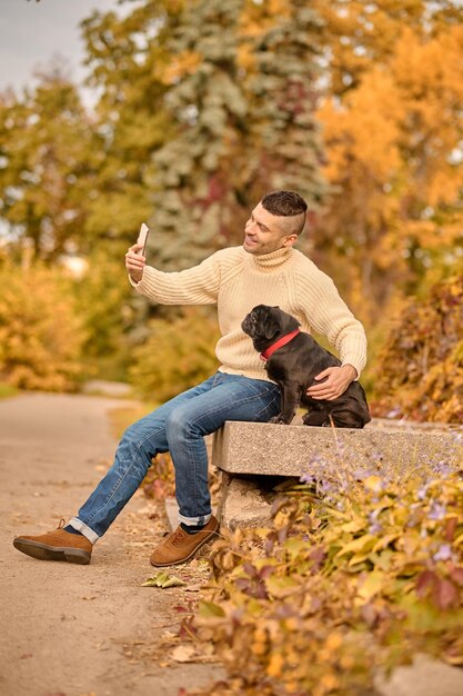 우정. 애완 동물과 함께 공원에서 쉬고 있는 베이지색 터틀넥을 입은 남자
