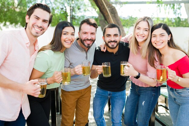 Воссоединение дружбы. Портрет привлекательной группы друзей в возрасте 20 лет, улыбающихся и смотрящих друг другу в глаза, гуляющих и наслаждающихся пивом