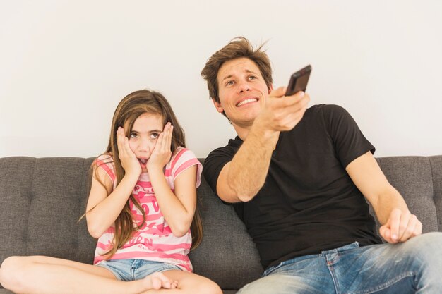 Frightened girl sitting with her father holding remote control