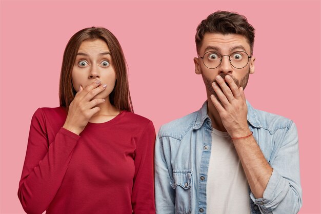 Frightened young couple posing against the pink wall