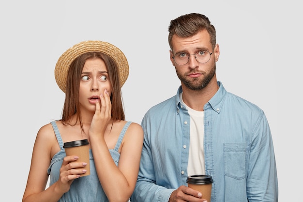 Free photo frightened young european woman in straw headgear looks fearful at his companion who has frustrated expression