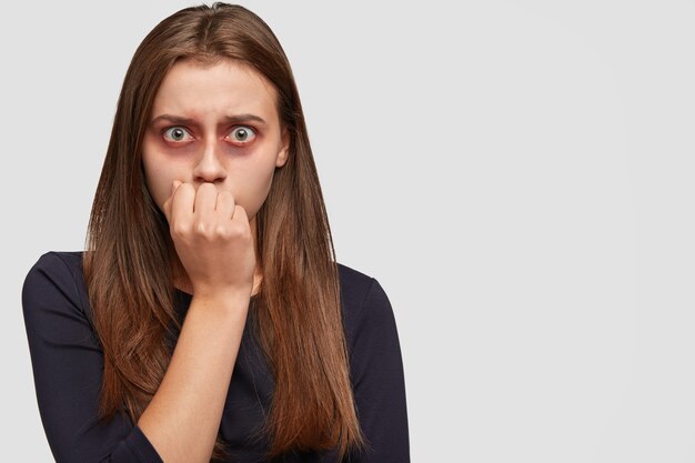 Frightened young woman with bruises posing against the white wall