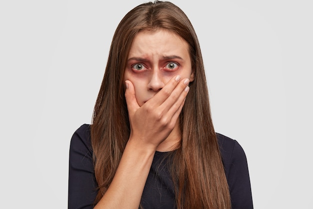 Frightened young woman with bruises posing against the white wall