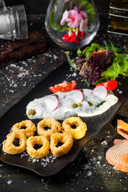 Бесплатное фото Сверху кольца кальмаров в кляре с салатом из свежих овощей и соусом и цветами в лотке
