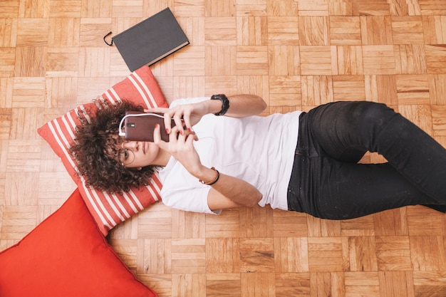 Сверху подросток с помощью смартфона на полу