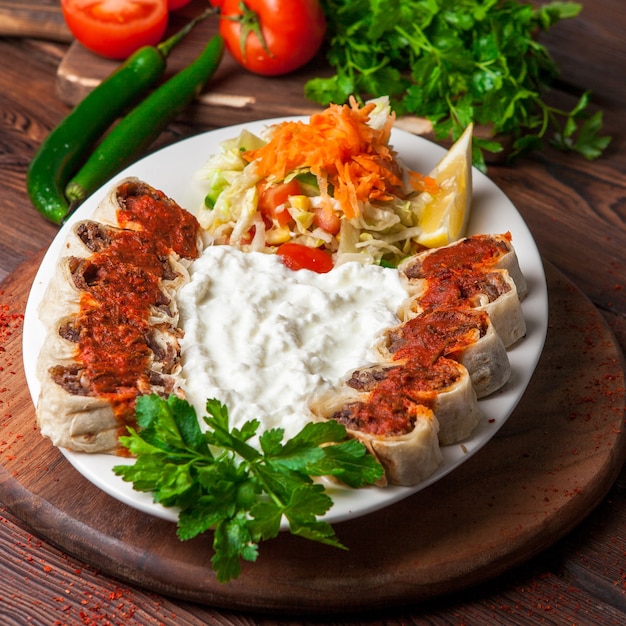 From above beyti kebab with yogurt and lemon and salad in white plate