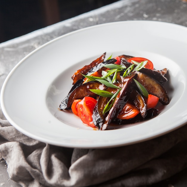 From above fried eggplant with tomato and chopped green onions and rag in round white plate