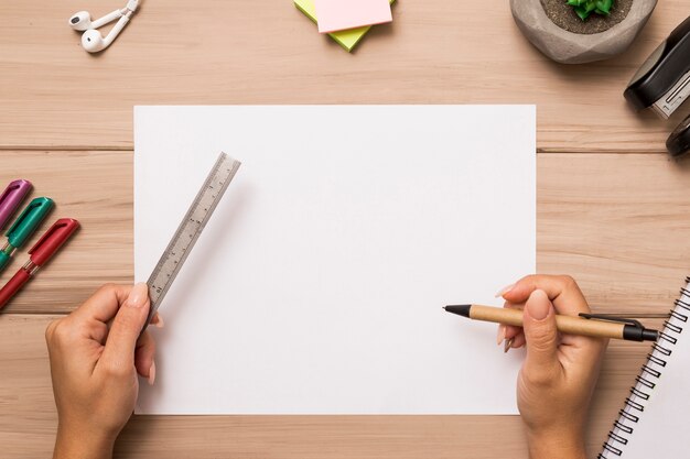 From above hands holding ruler and pen over blank paper sheet