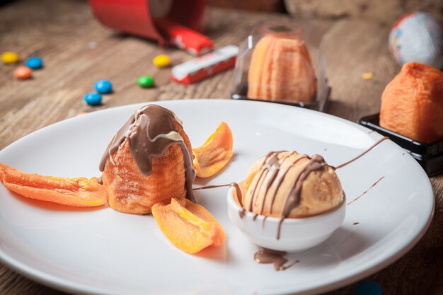 上からチョコレートシロップとドライアプリコットの丸い白いプレートのアイスクリーム