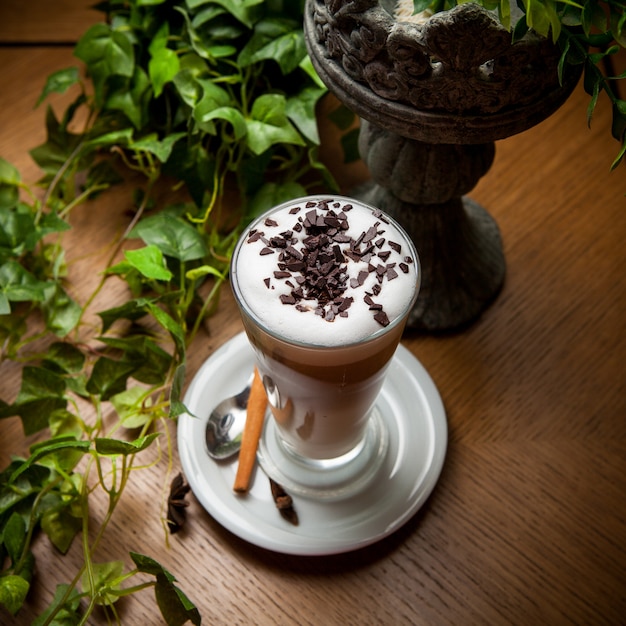 From above latte with cinnamon and chocolate chips and grape branch in glass cup