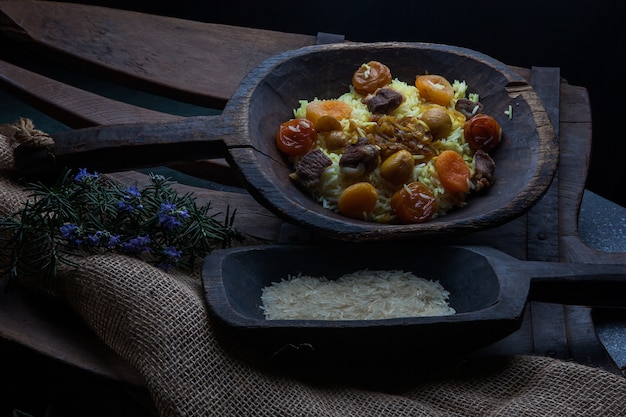 Dall'alto pilaf con raduno e frutta secca e castagne e riso e foglie di rosmarino in un piatto di legno