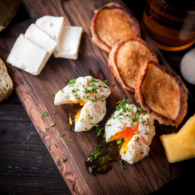 Free photo from above poached egg with pancakes and cup of tea and cheese in board cookware