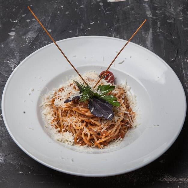 From above spaghetti with tomato and greens and ricotta cheese in round white plate