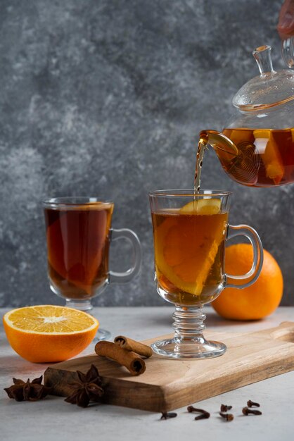 From transparent glass teapot pour tea in glass mug.