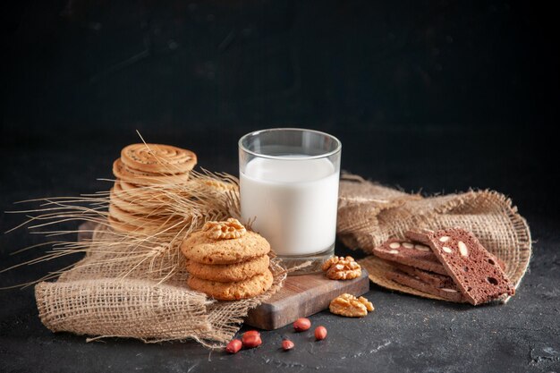Fron close view of a fresh milk in a glass cookies spikes on nude color towel walnuts peanuts on black wave background