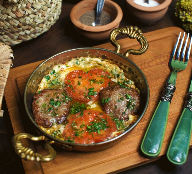 A front close up view cooked eggs along with red tomatoes inside metallic pan on the brown wooden desk