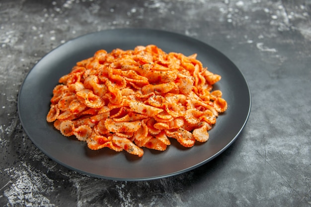 Vista ravvicinata frontale di un delizioso pasto di pasta su un piatto nero per cena su sfondo scuro